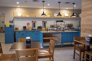 A modern cafe with blue cabinets, wooden tables, and hanging pendant lights.
