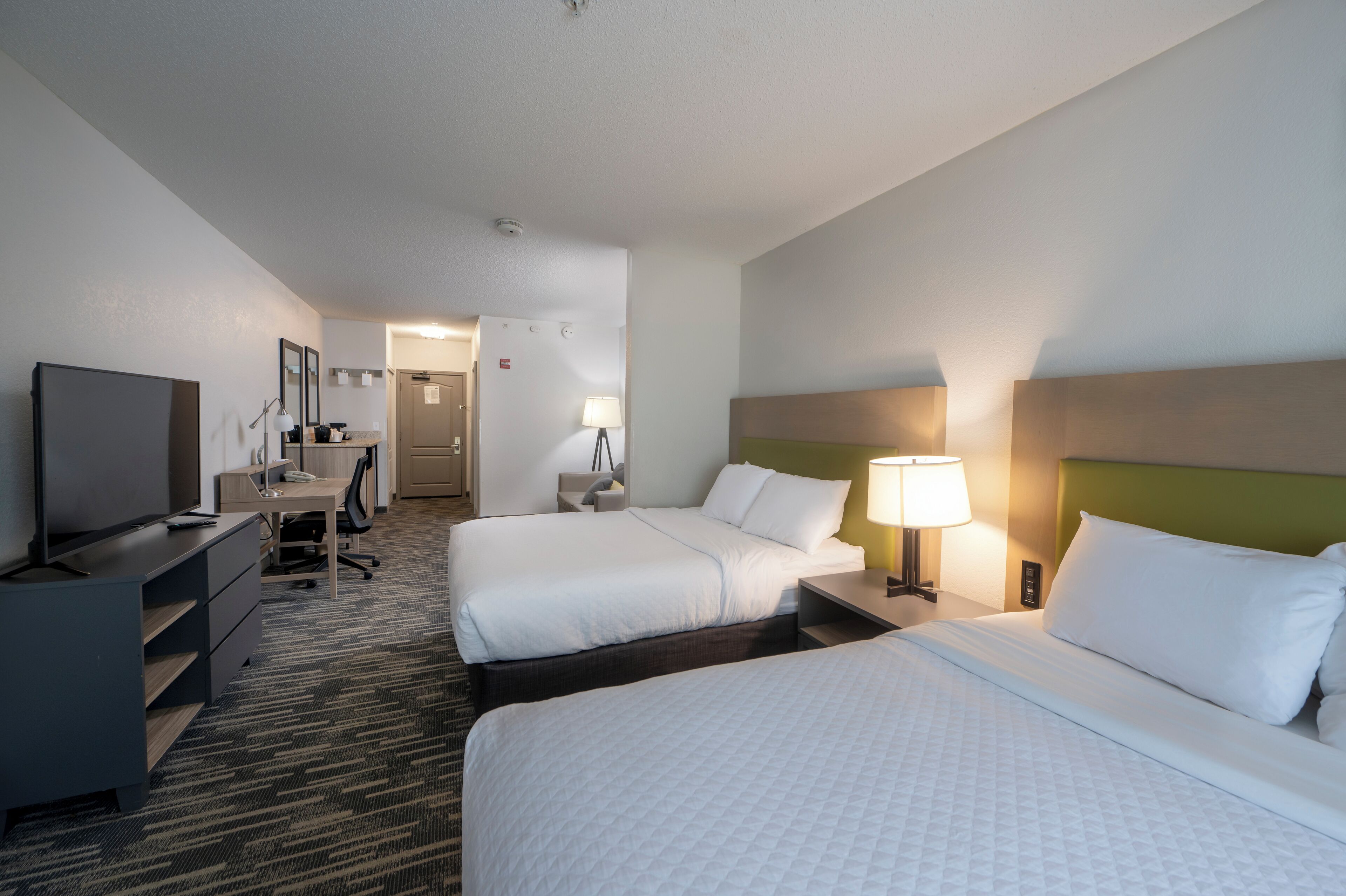 A hotel room with two beds, a desk, a television, and a bathroom visible in the background.