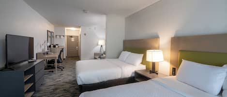 A hotel room with two beds, a desk, a television, and a bathroom visible in the background.