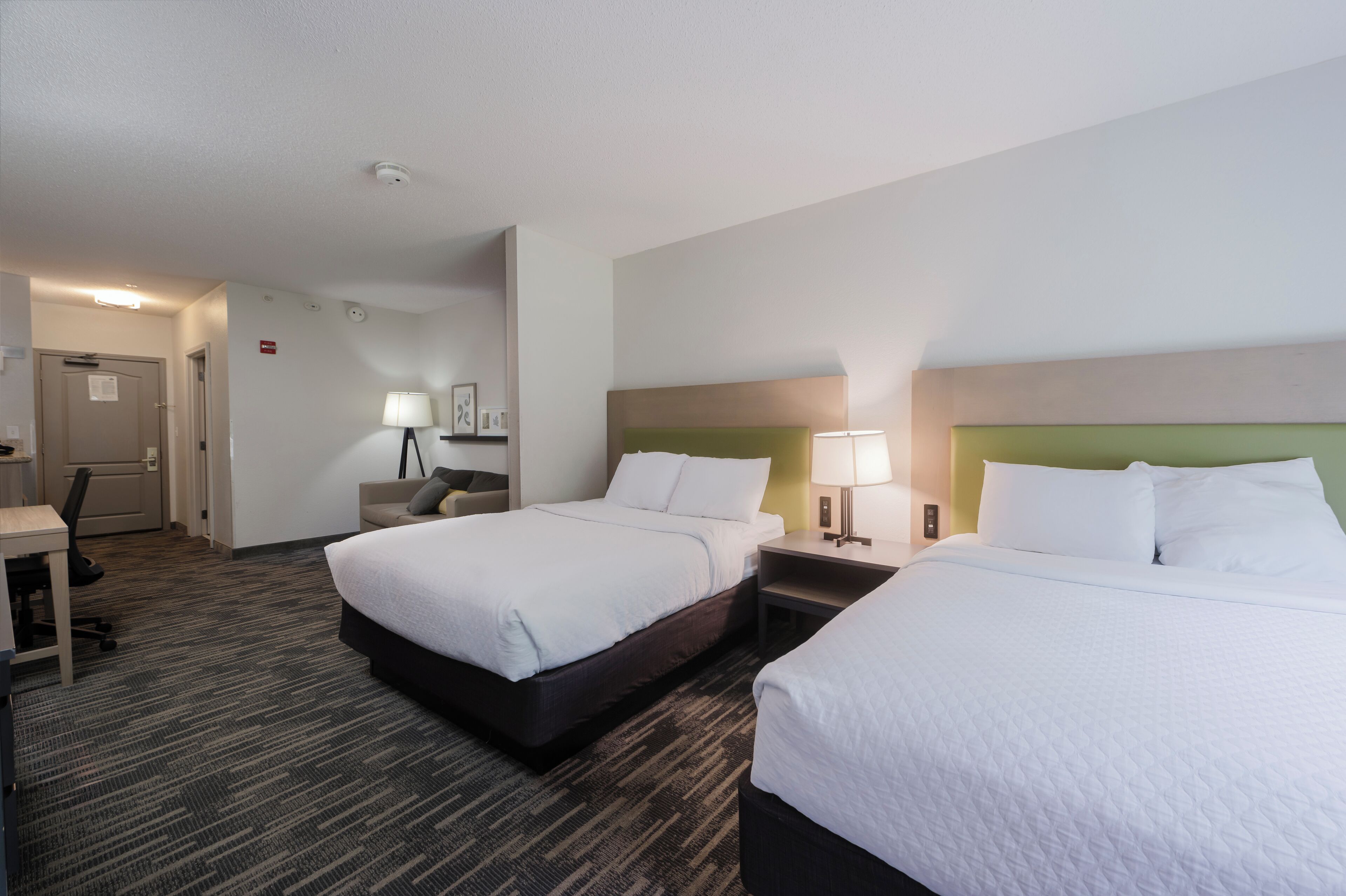 A hotel room with two beds, a desk, and a chair.