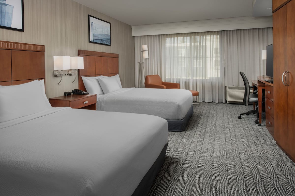A hotel room with two beds, a desk, a chair, a TV, and a window with curtains.