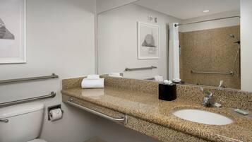 Un baño moderno con encimera de granito, lavamanos, inodoro y zona de ducha.