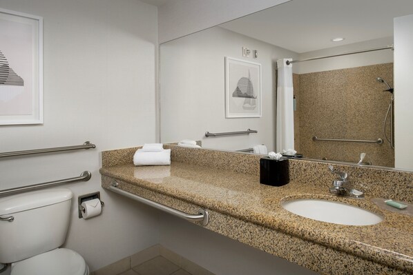 Un baño moderno con encimera de granito, lavamanos, inodoro y zona de ducha.