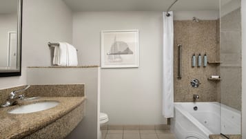A modern bathroom with a granite countertop sink, a toilet, a framed artwork on the wall, and a shower area with a glass door.