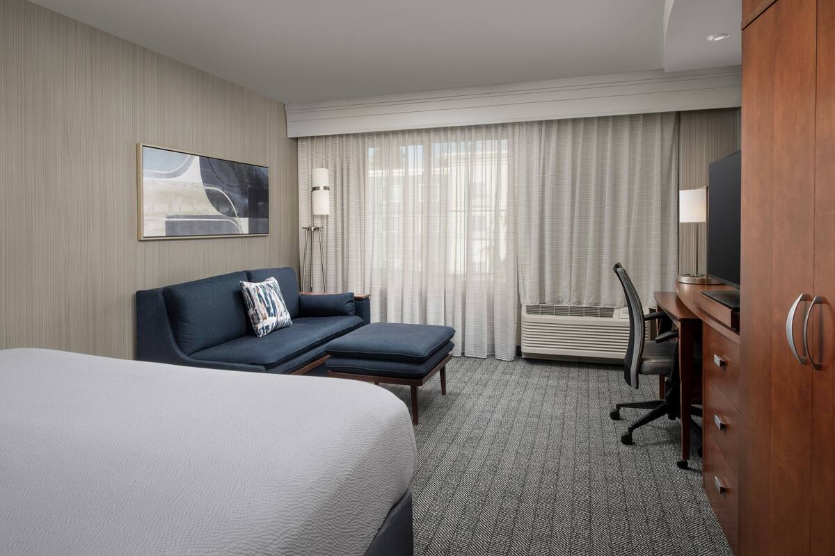 A hotel room with a large bed, a sofa, a desk, and a television.