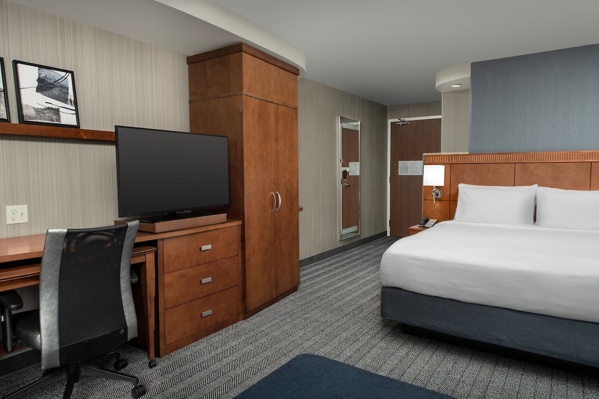 A hotel room with a large bed, a desk with a television, a chair, and a wardrobe.