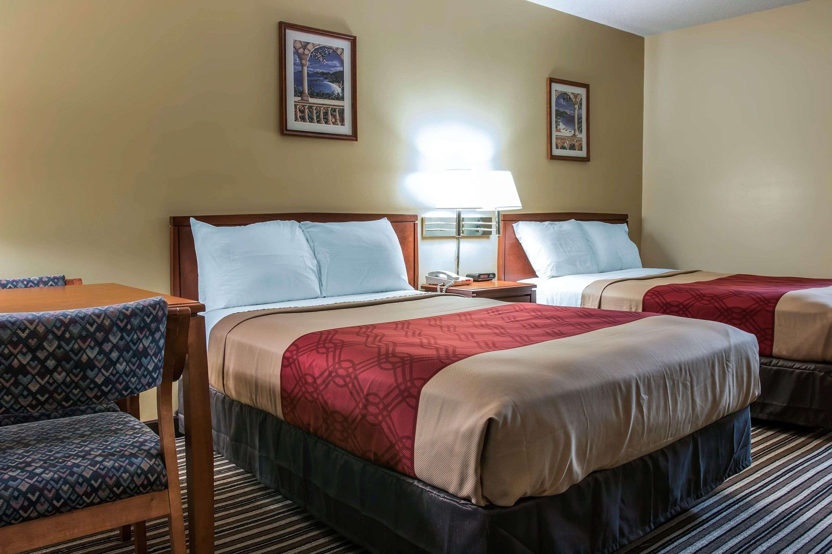 A hotel room with two beds, a desk, and chairs. There are two framed pictures on the wall.