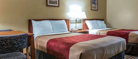 A hotel room with two beds, a desk, and chairs. There are two framed pictures on the wall.