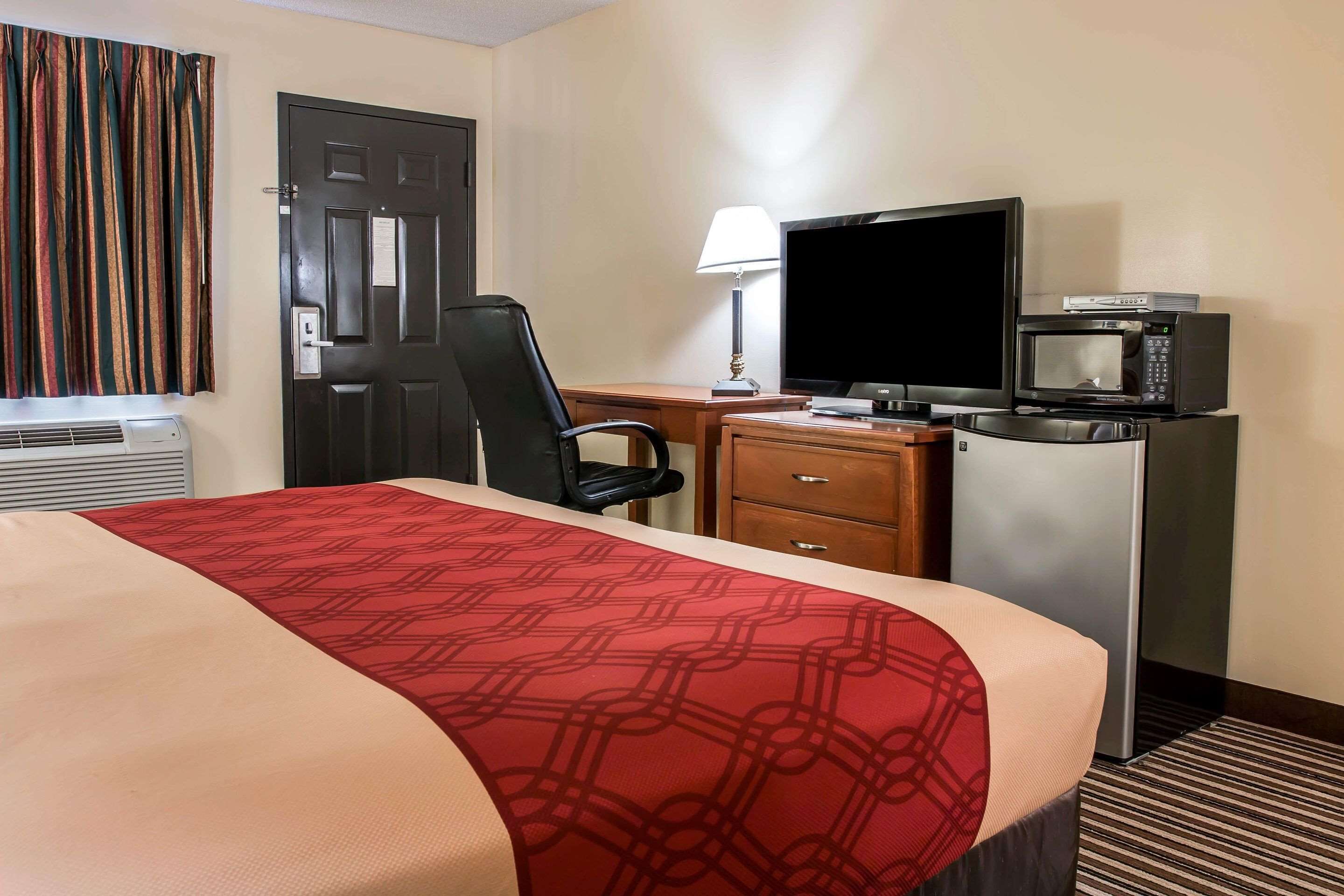 A hotel room with a bed, a desk, a chair, a television, a microwave, and a door.