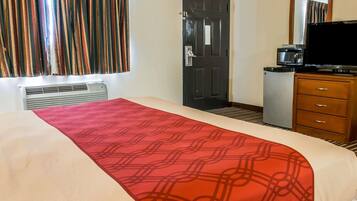 A hotel room with a bed, a television, a microwave, and a small refrigerator.