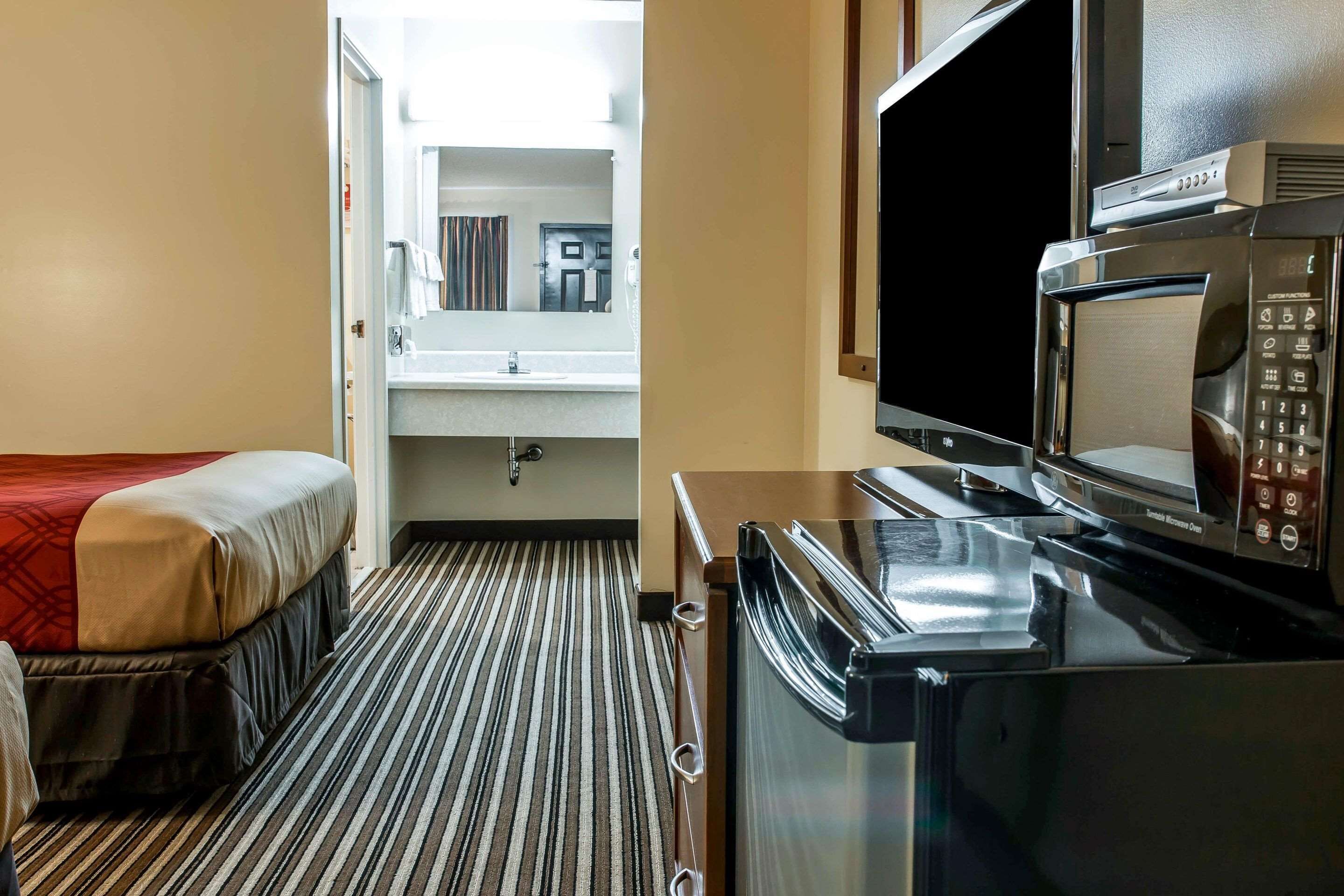 Een hotelkamer met een bed, een kitchenette met een magnetron, en een badkamer door een geopende deur zichtbaar.