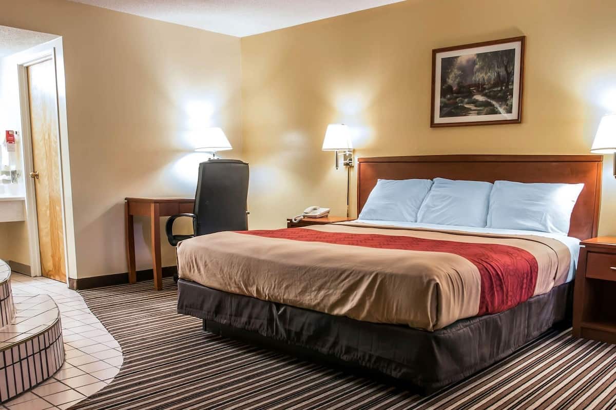 Ein Hotelzimmer mit einem Bett, zwei Nachttischlampen, einem Schreibtisch mit Stuhl, einem Telefon und einem Bild an der Wand.