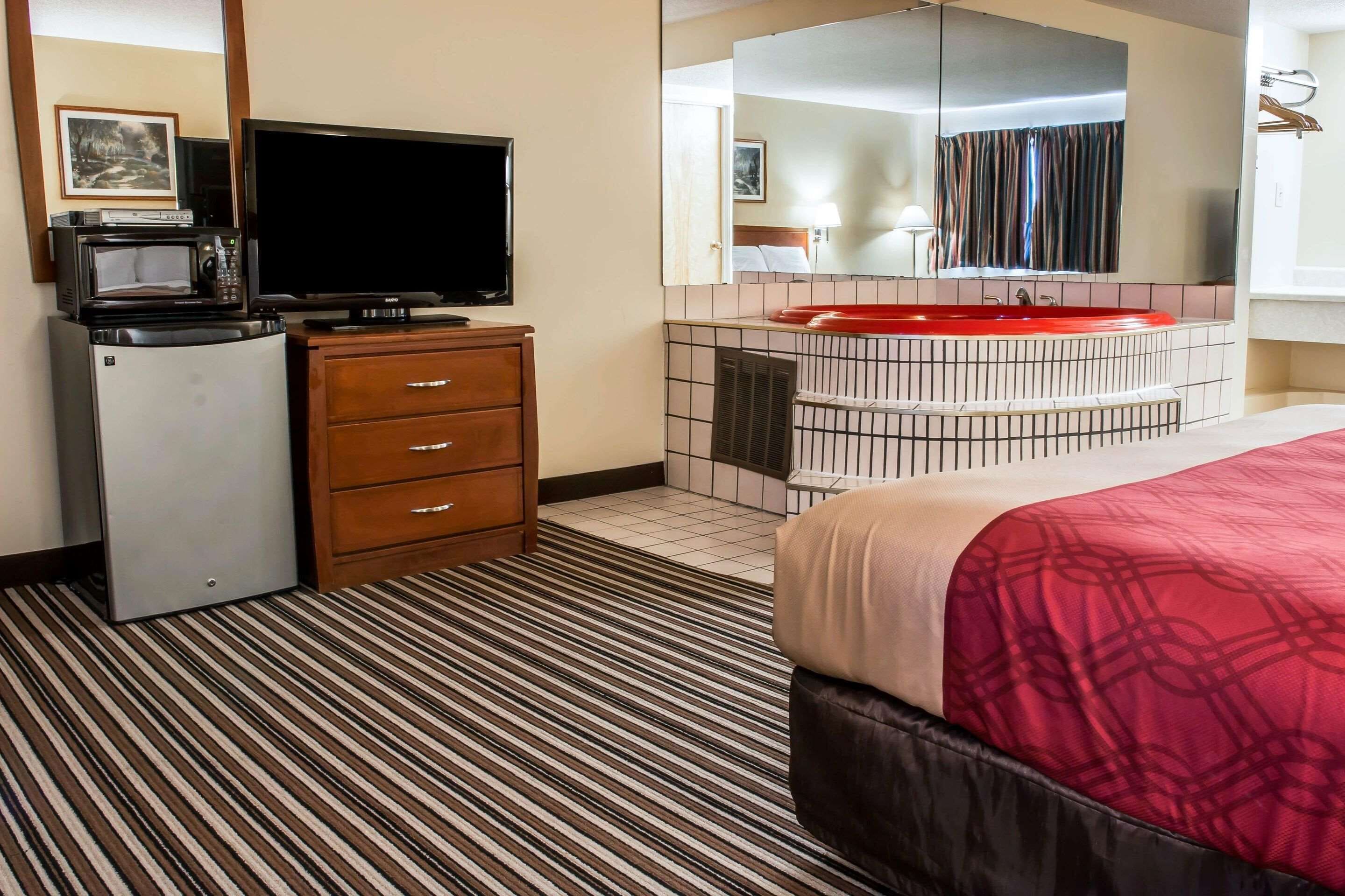 Hotelkamer met een bed, een televisie, een magnetron, een koelkast, een wastafel met spiegel en een rode wasbak.