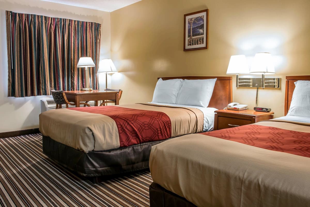 Ein Hotelzimmer mit zwei Betten, einem Schreibtisch, einem Stuhl, einer Lampe und einem Nachttisch mit Telefon.