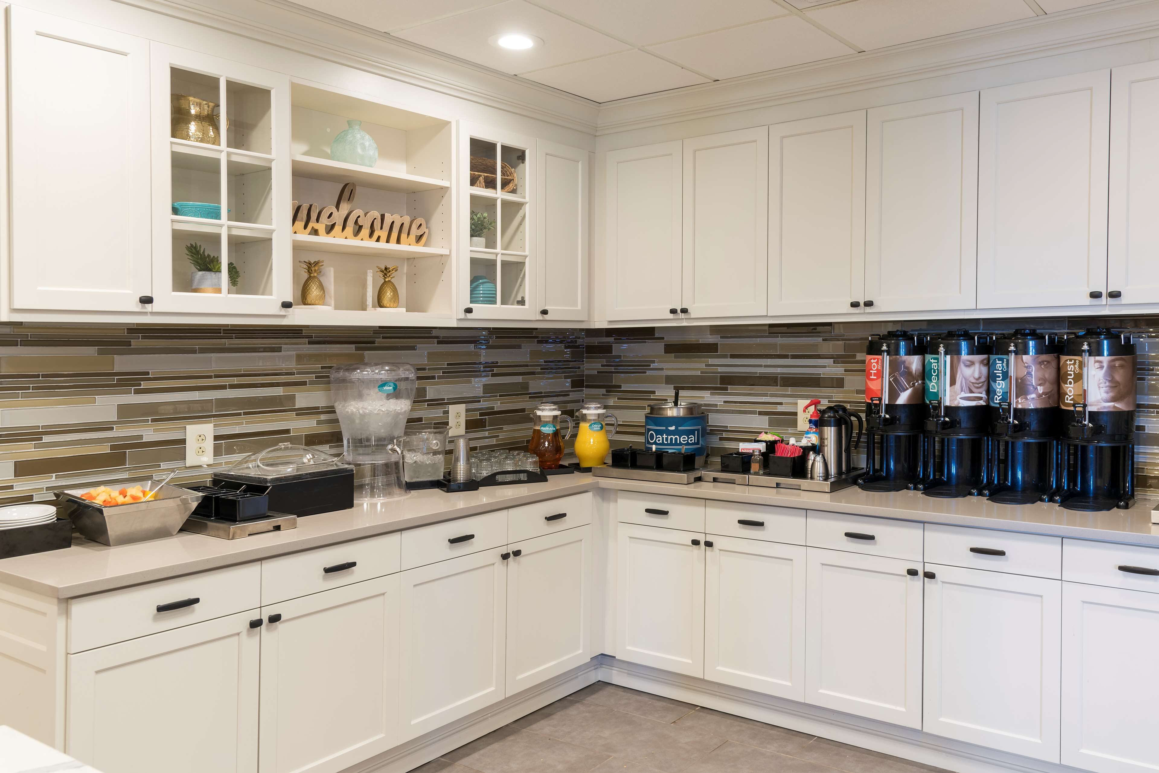 A modern kitchen with white cabinets, a tiled backsplash, and a coffee station with multiple dispensers.