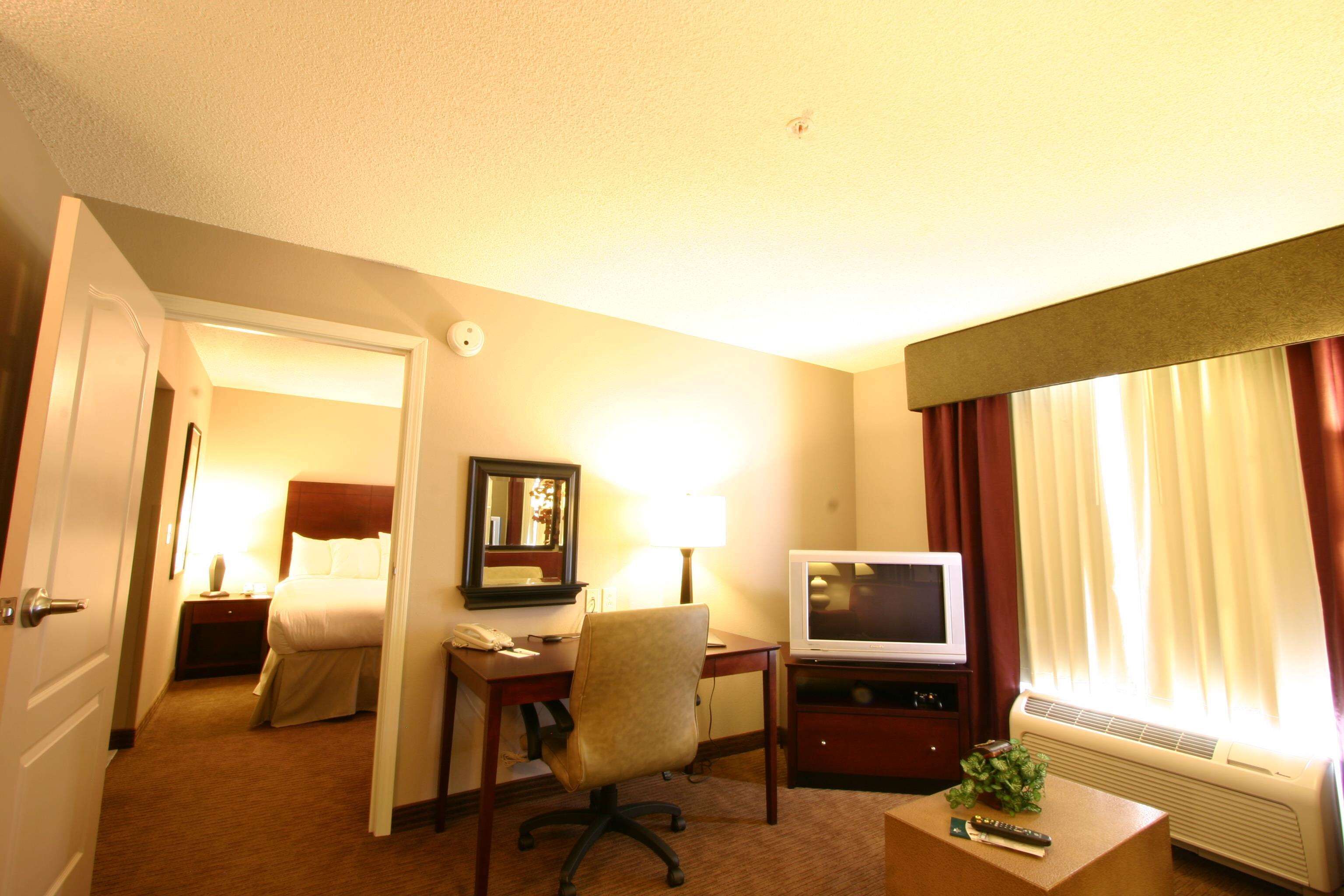 Habitación de hotel con cama, escritorio, teléfono, lámpara, televisión y una silla.