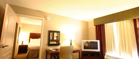 Habitación de hotel con cama, escritorio, teléfono, lámpara, televisión y una silla.