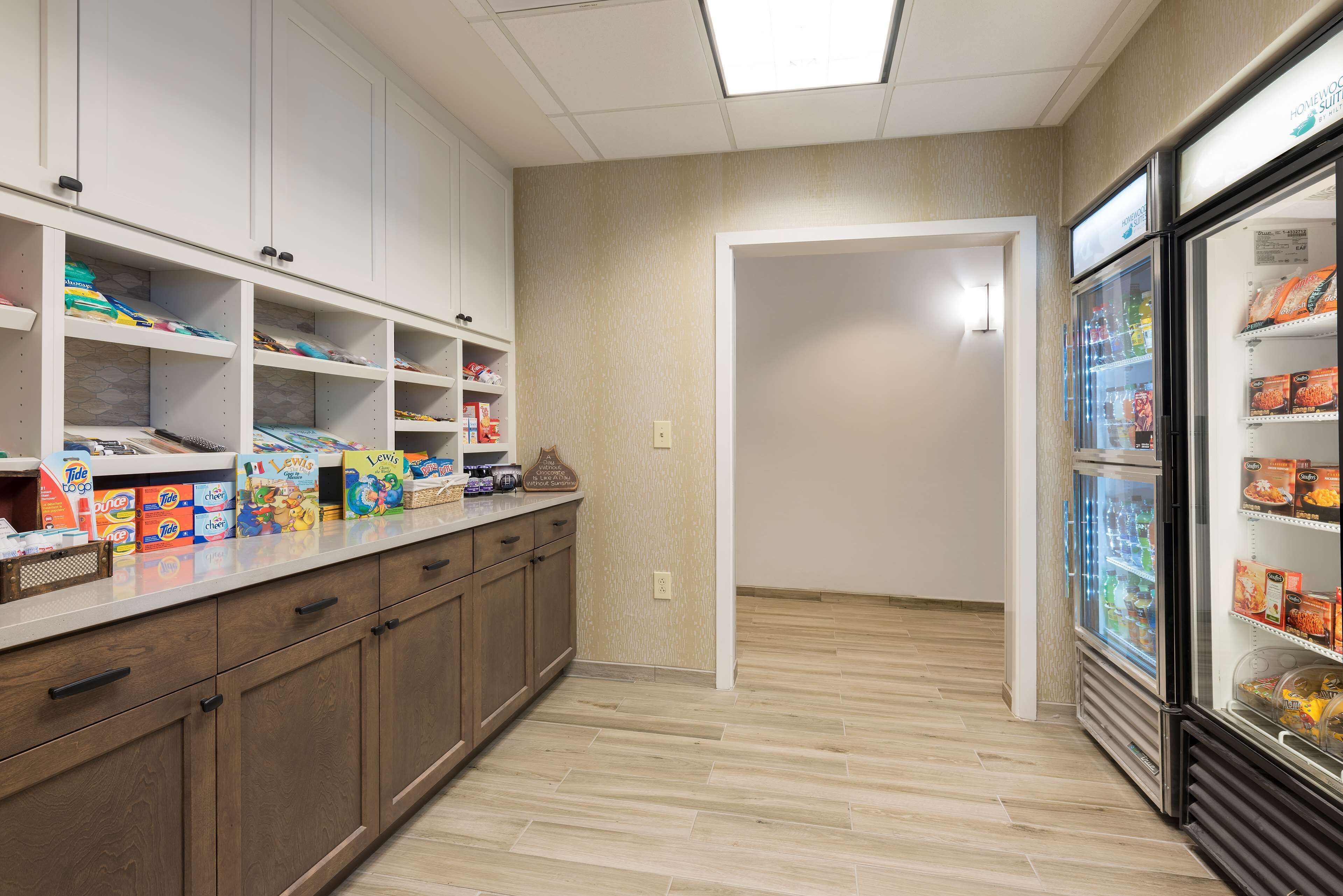 A kitchen area with wooden cabinets, a countertop with various food items, and a refrigerator stocked with beverages.