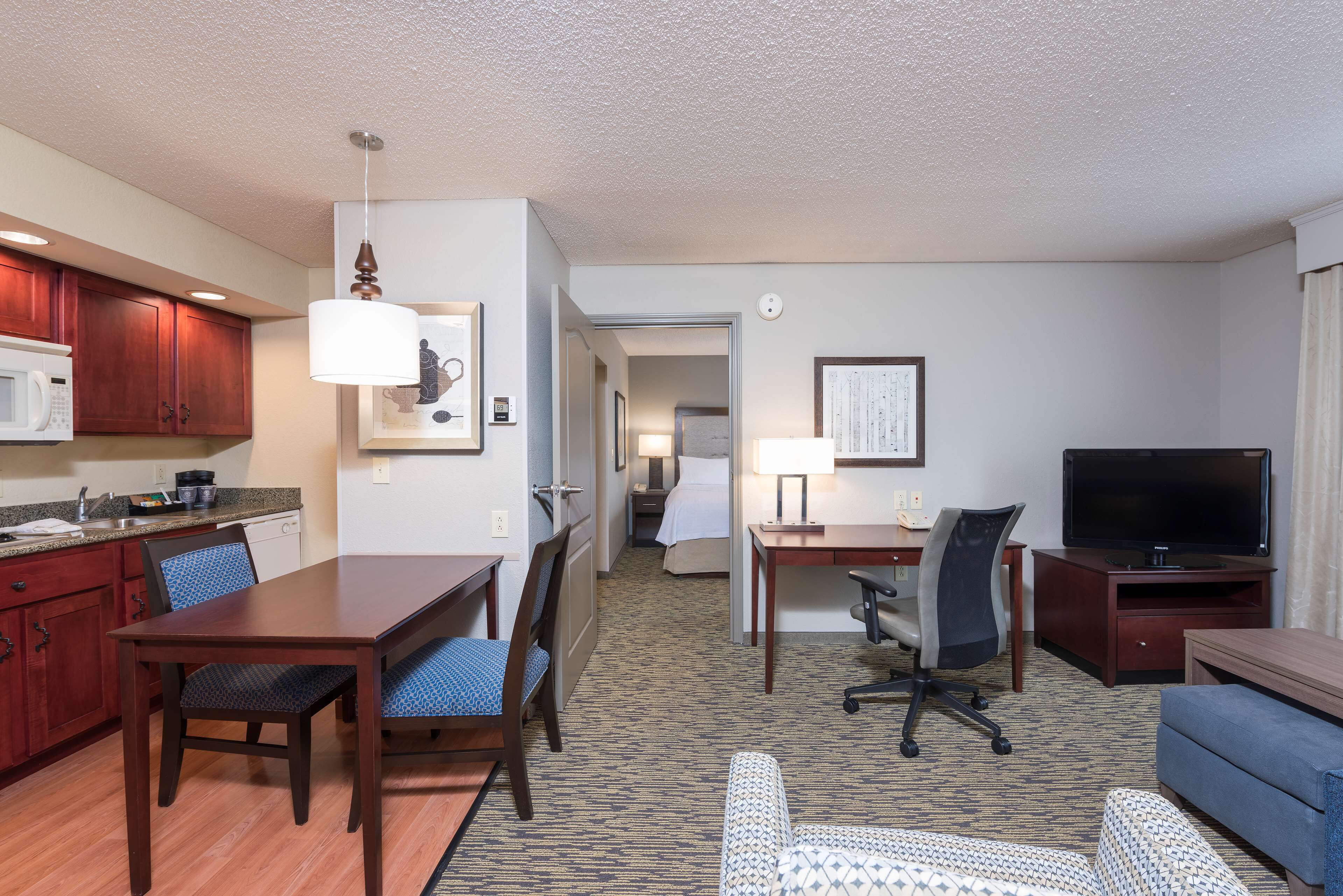 Habitación de hotel con una mesa de comedor, sillas, televisor, sofá y una zona de cocina con microondas y armarios.