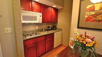 A compact kitchen with red cabinets, a white microwave, a coffee maker, and a sink.