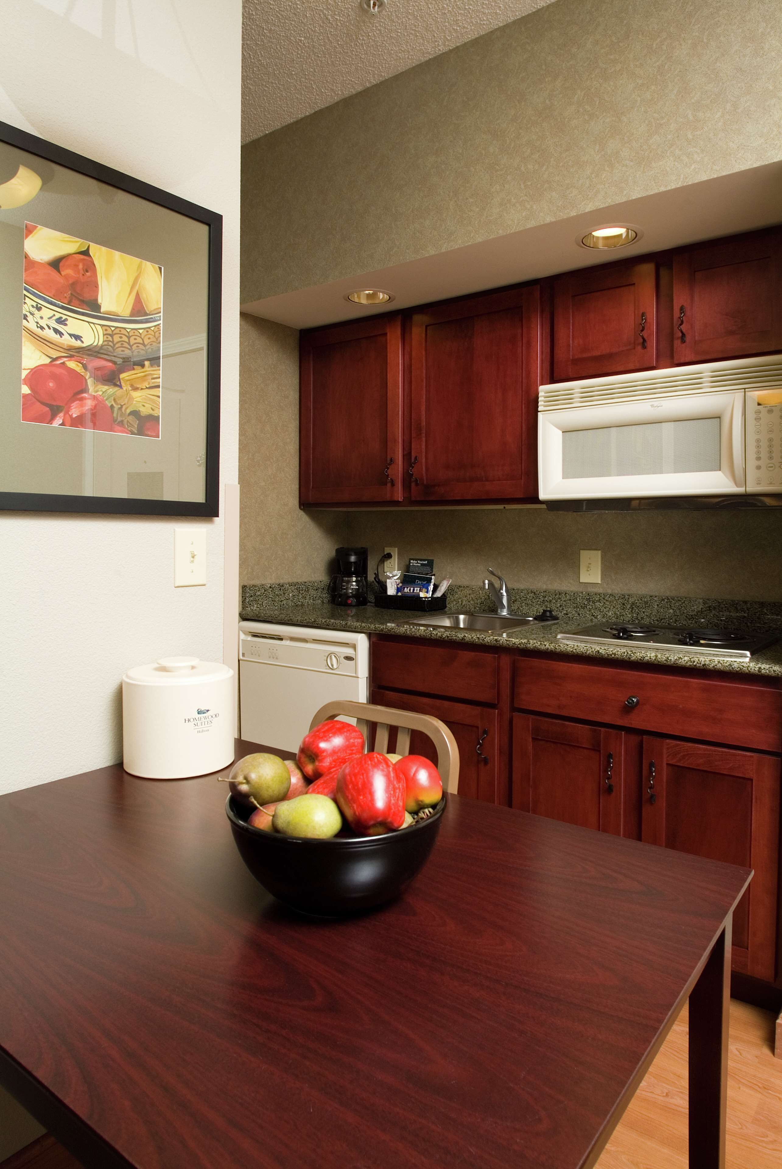 A kitchen with wooden cabinets, a microwave, a dishwasher, and a fruit bowl on the counter.