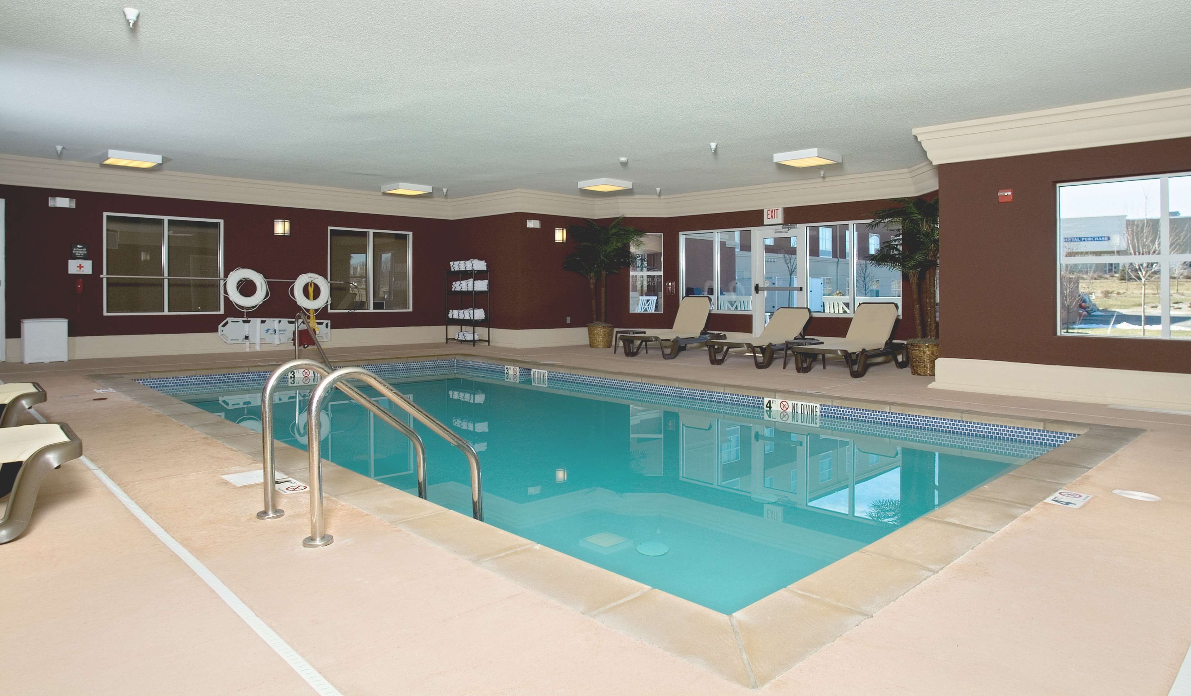 Una piscina interior con un puesto de socorrista, una escalera de piscina y sillones de descanso junto a la piscina.