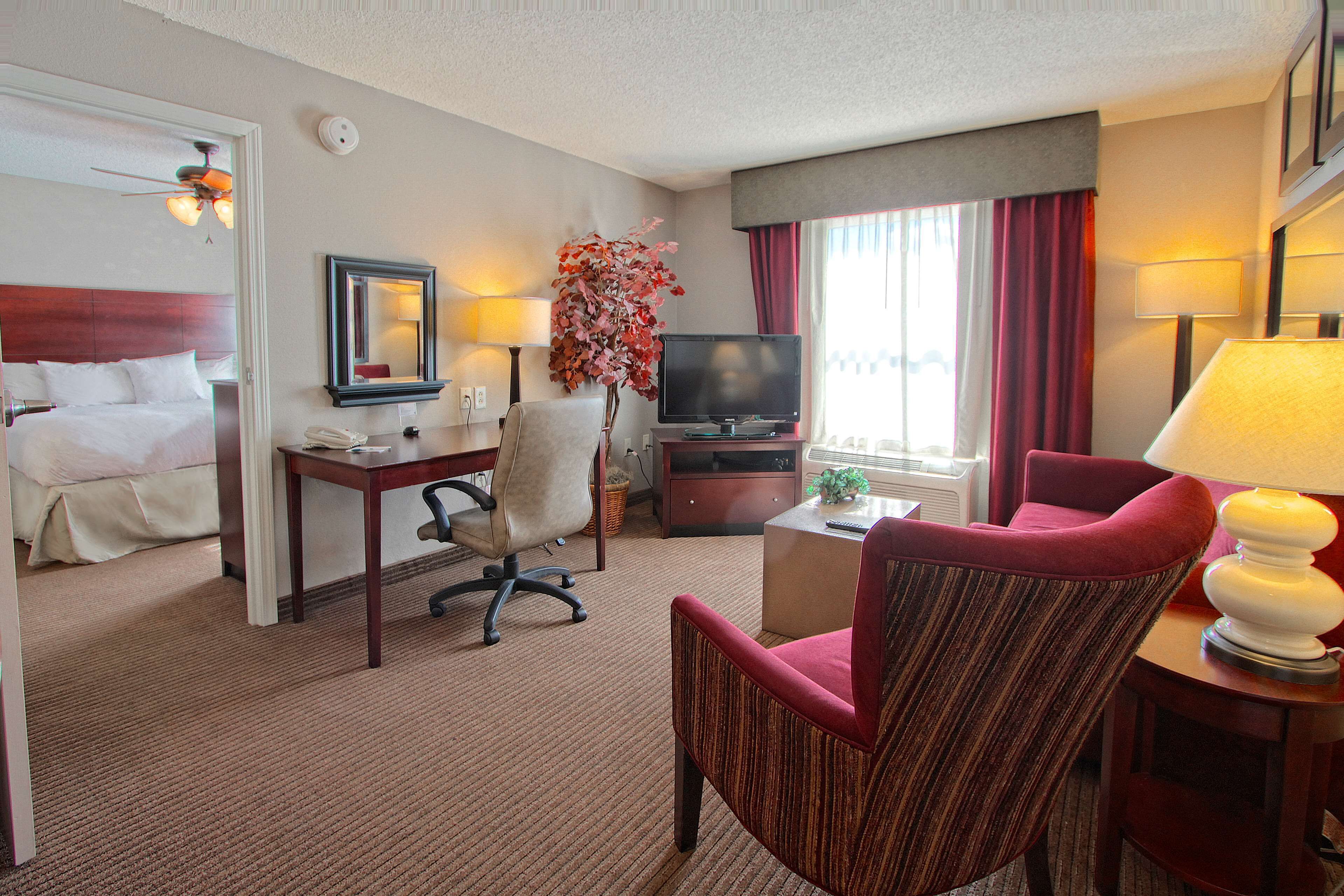 A hotel room with a bed, desk, chair, television, and a window with curtains.