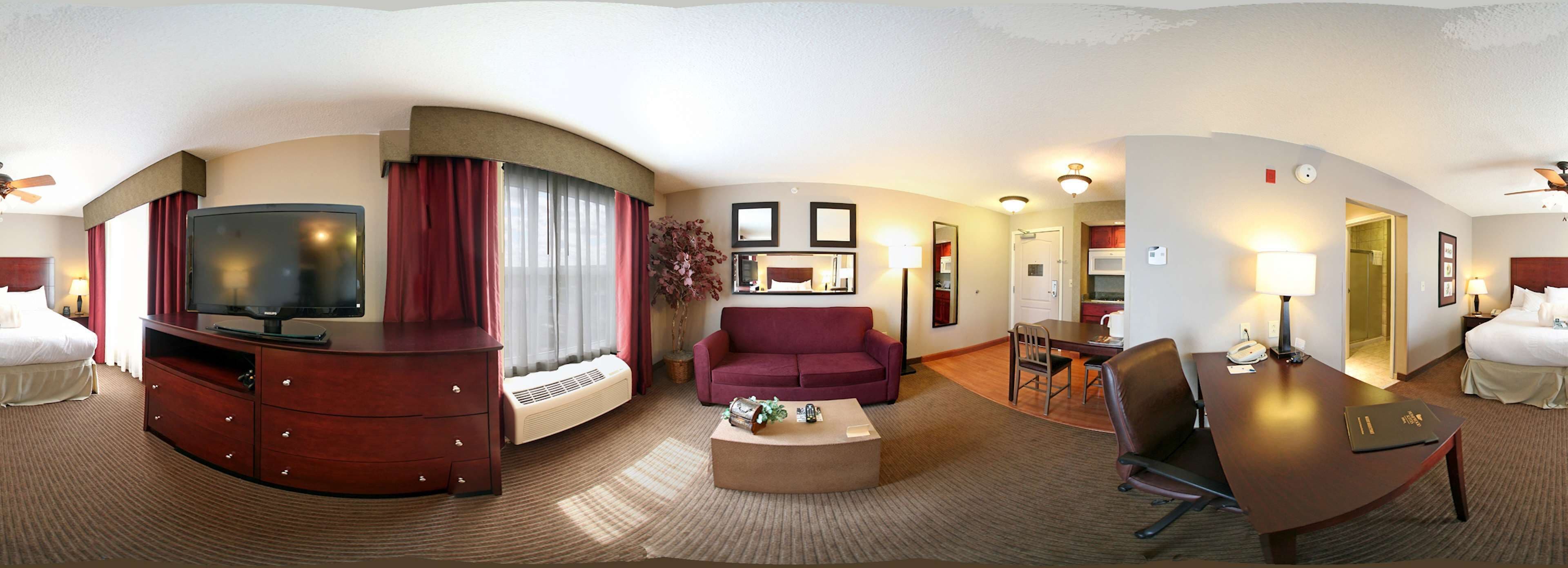 A hotel room with a TV, a sofa, a coffee table, a dining table with chairs, and a bathroom visible through an open door.