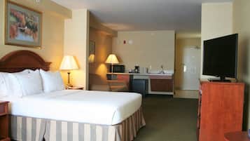 Habitación de hotel con cama, lámparas de noche, televisor, escritorio con computadora y una pequeña cocina.