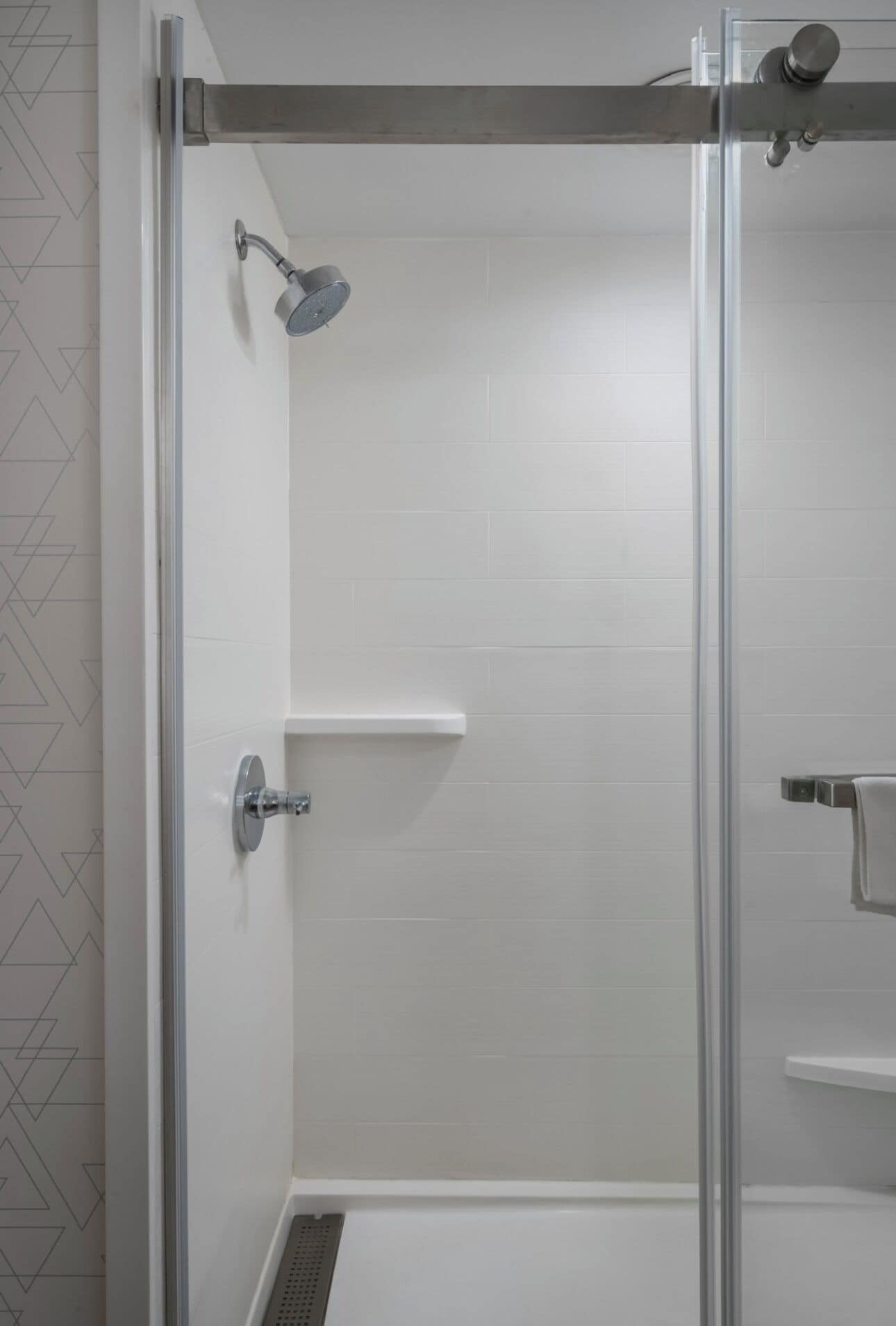 A glass-enclosed shower with a handheld showerhead, a wall-mounted towel rack, and a small shelf.