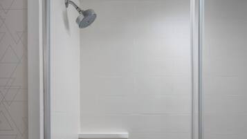 A glass-enclosed shower with a handheld showerhead, a wall-mounted towel rack, and a small shelf.
