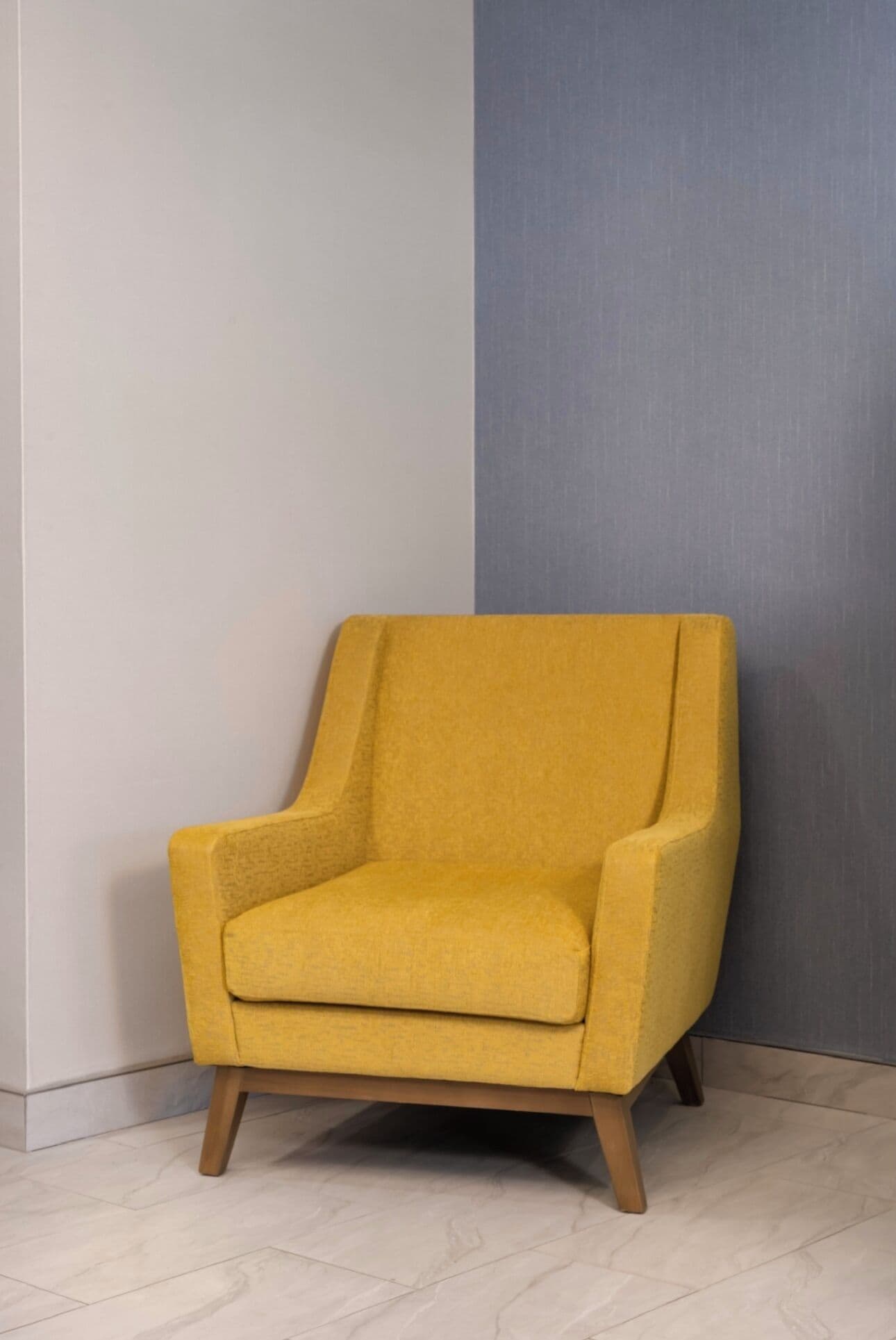 Un sillón amarillo con patas de madera, ubicado frente a una pared con un panel gris.