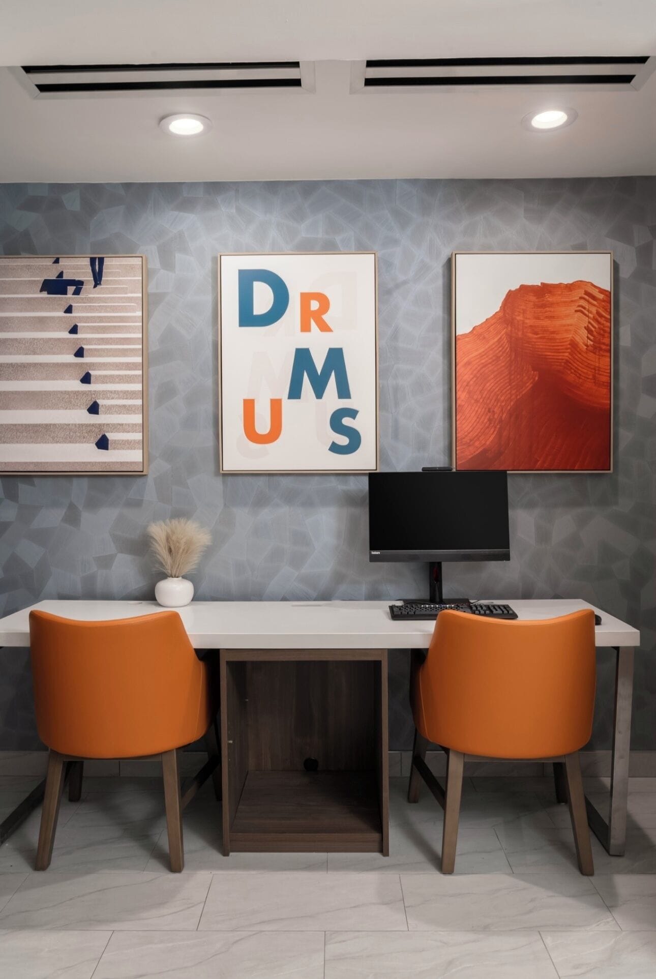 A modern office space with a desk, two chairs, a monitor, and artwork on the wall.