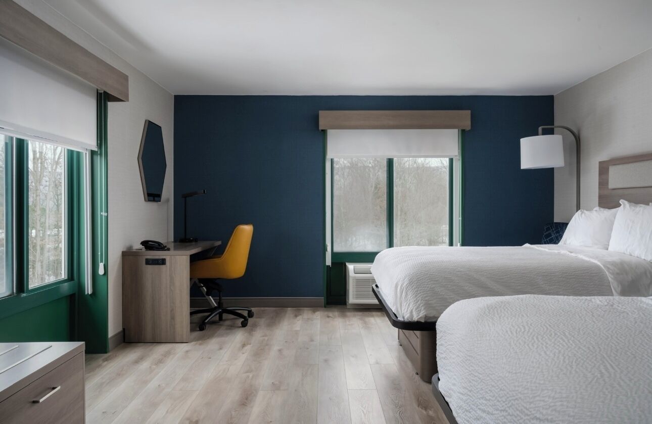 Una habitación de hotel con cama, escritorio, silla y lámpara.