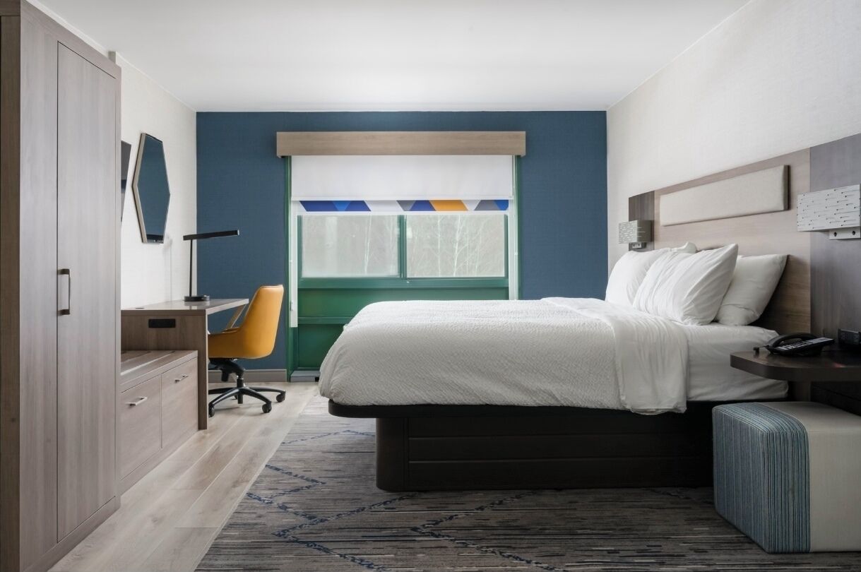 Une chambre à coucher comprenant un lit, une table de chevet, une chaise, un bureau, une armoire et une fenêtre avec des stores.