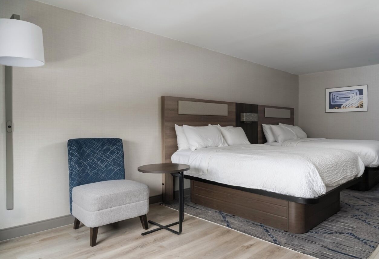 A hotel room with a bed, a chair, a small table, and a lamp.