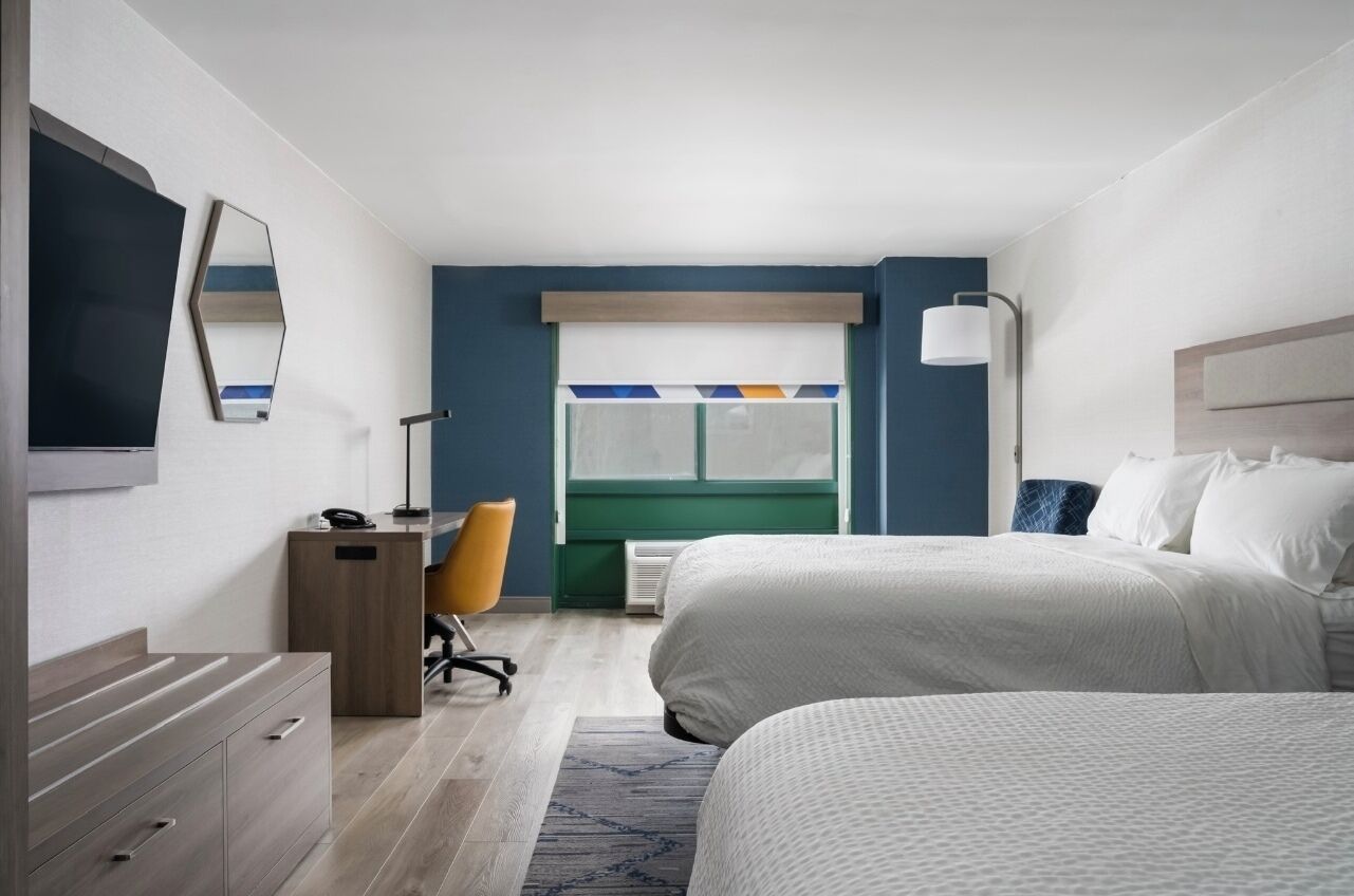 Una habitación de hotel moderna con cama, escritorio, silla y un ventanal grande.