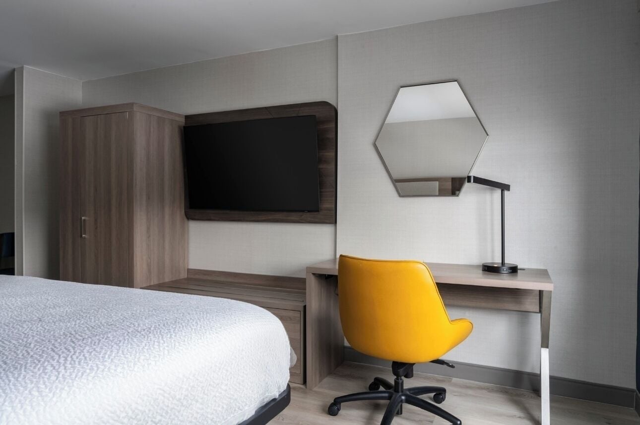 A hotel room with a bed, a desk with a chair, a TV, and a mirror.
