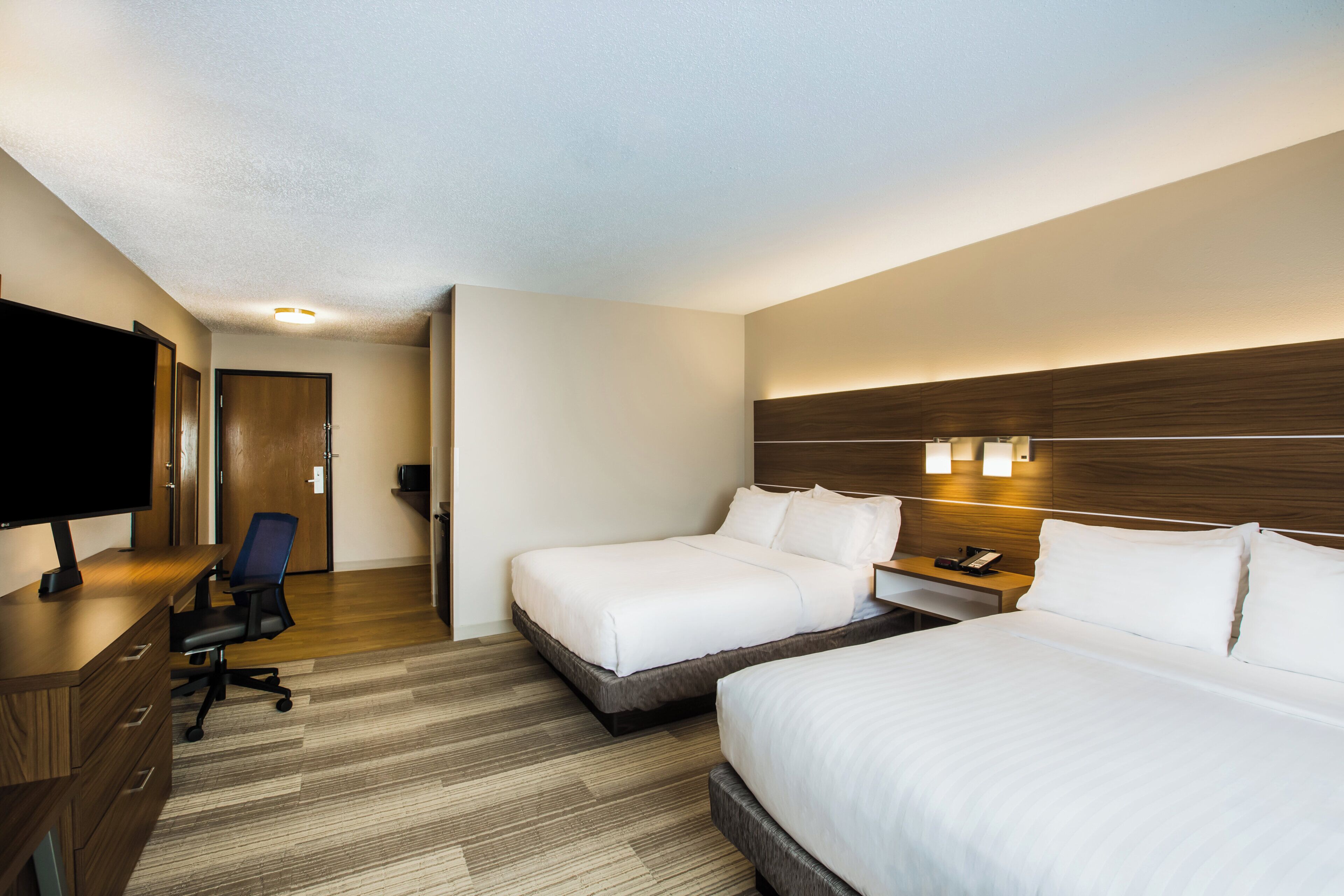 A hotel room with two beds, a desk, a chair, a television, and a nightstand.