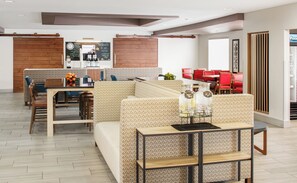 Un moderno vestíbulo de hotel con una zona de estar, un espacio para café y vistas a la cocina.