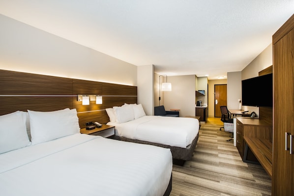 A hotel room with two beds, a desk, a chair, a television, and a wardrobe.