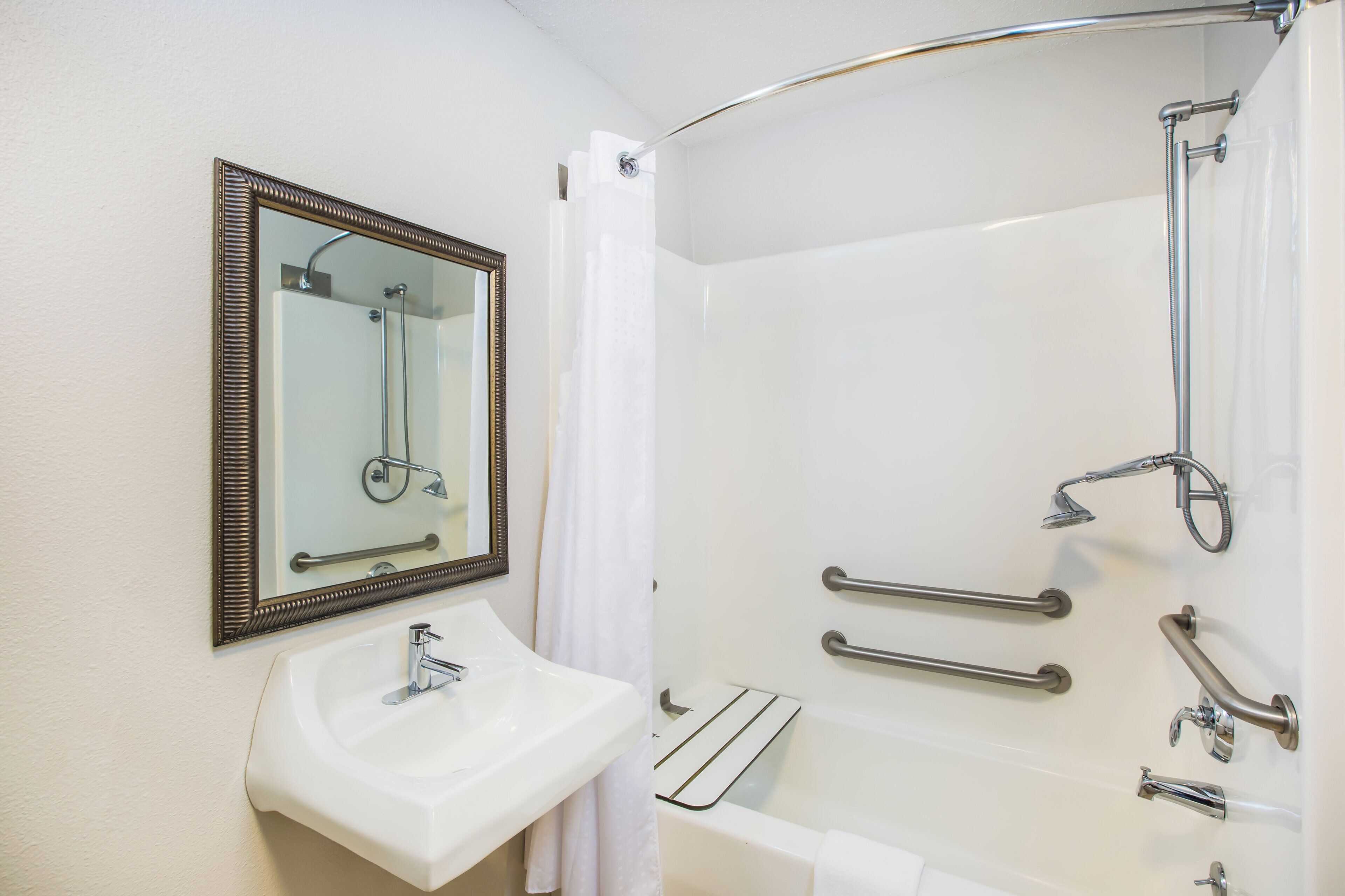 A bathroom with a sink, mirror, shower, and grab bars.