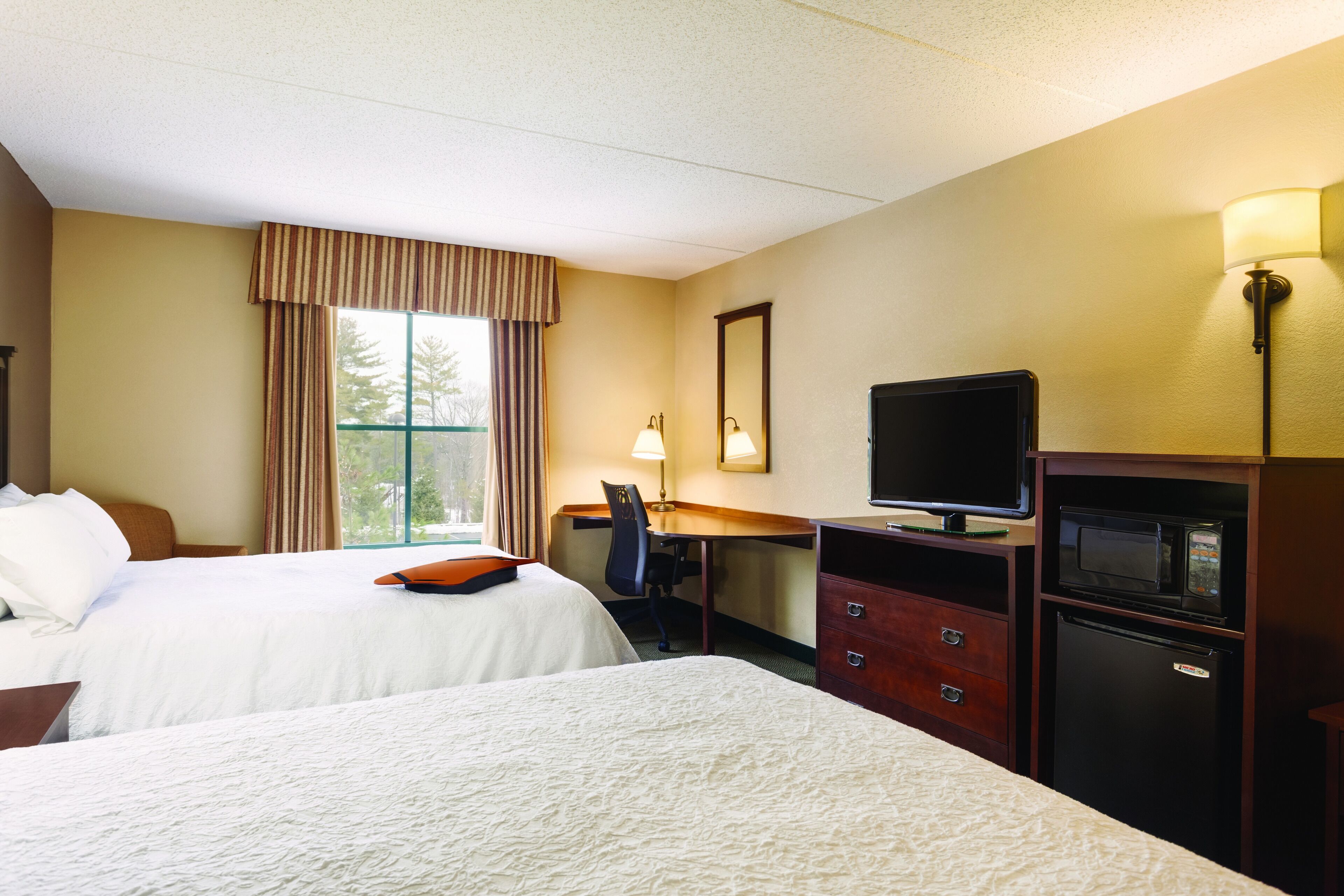 A hotel room with two beds, a desk with a computer, a television, and a refrigerator.