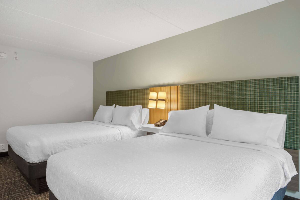 Quarto de hotel com duas camas, cabeceira com luminária e mesa pequena com telefone.