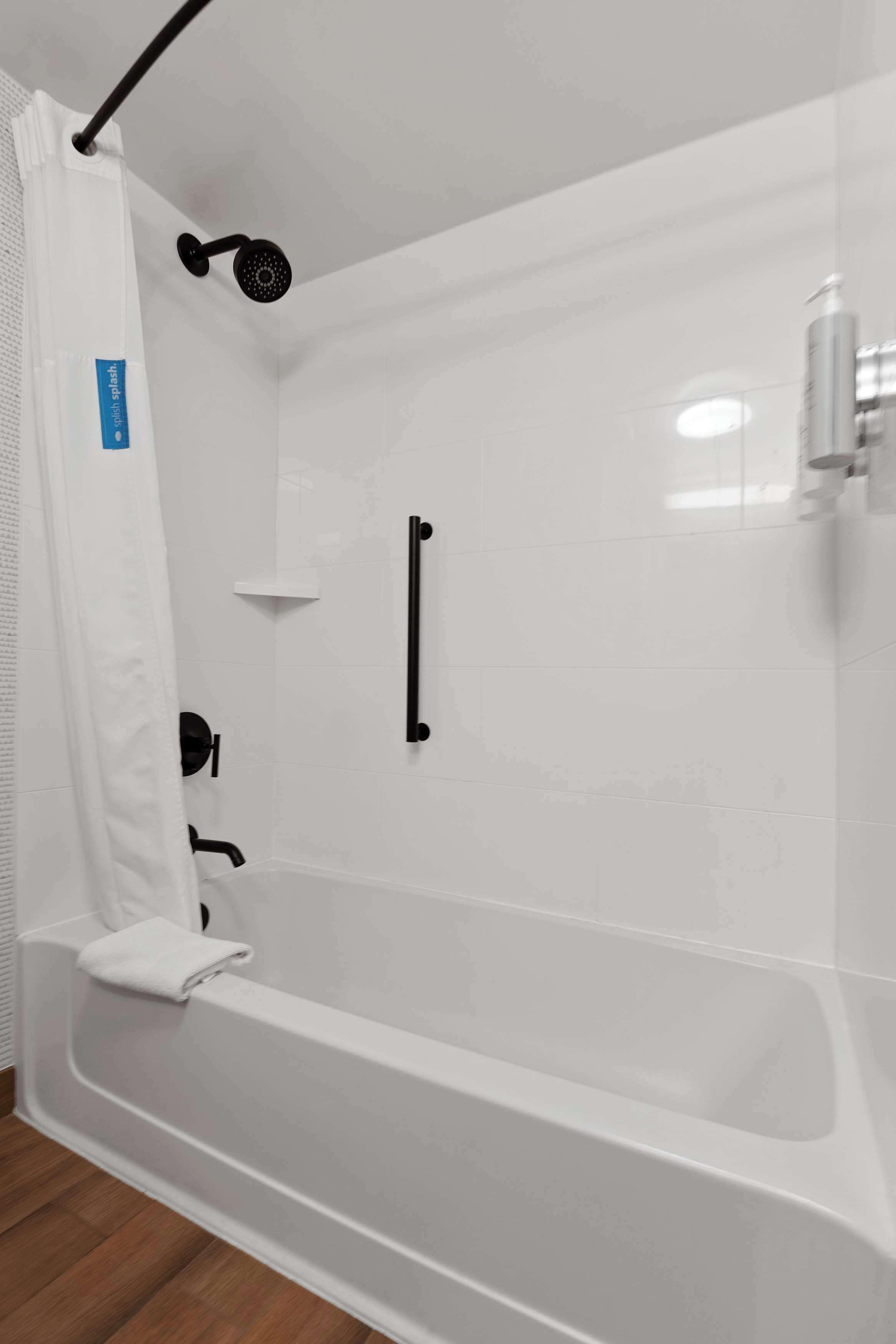 A modern bathroom with a white bathtub, a black showerhead, and a white shower curtain.