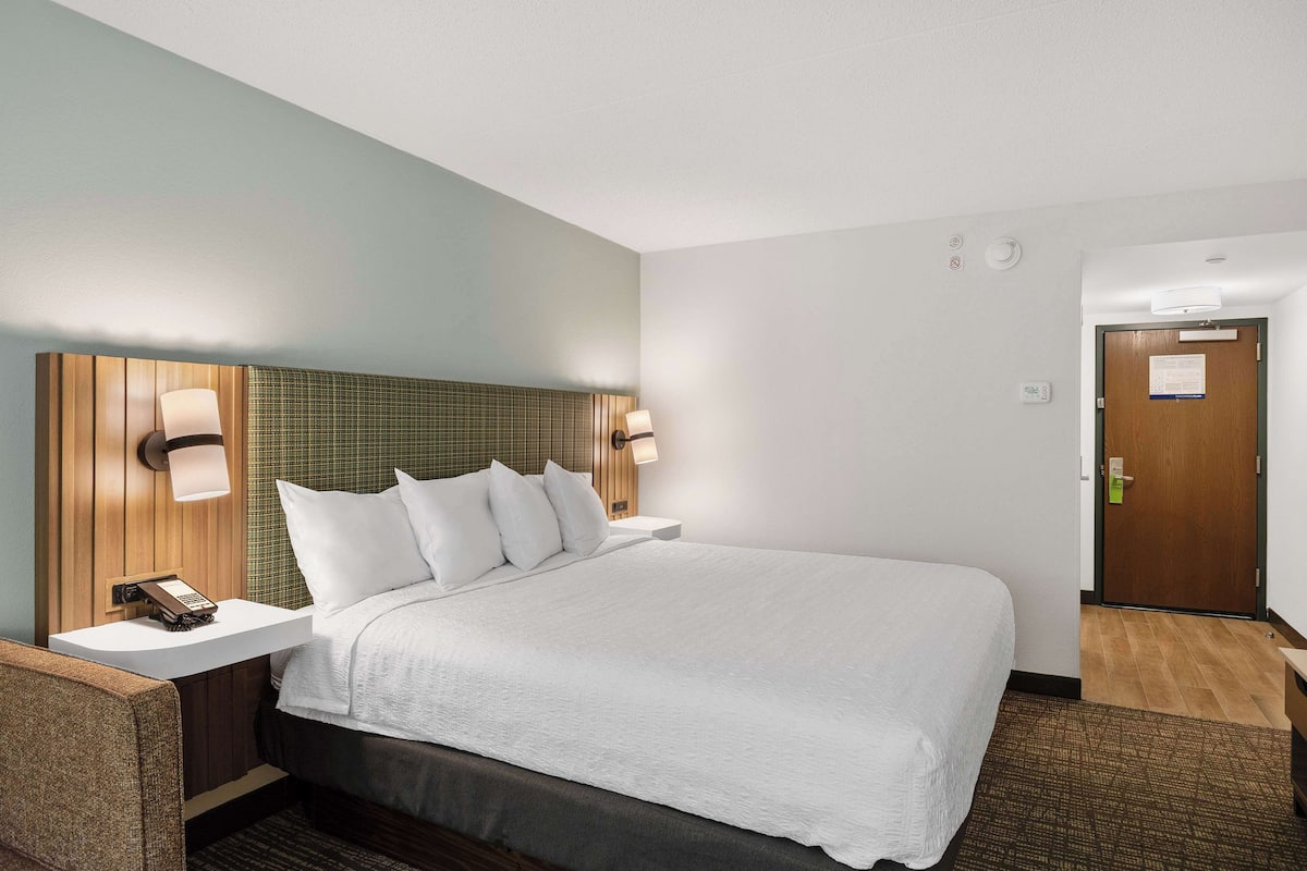 Quarto de hotel com cama, mesa de cabeceira, luminária e porta com um aviso.
