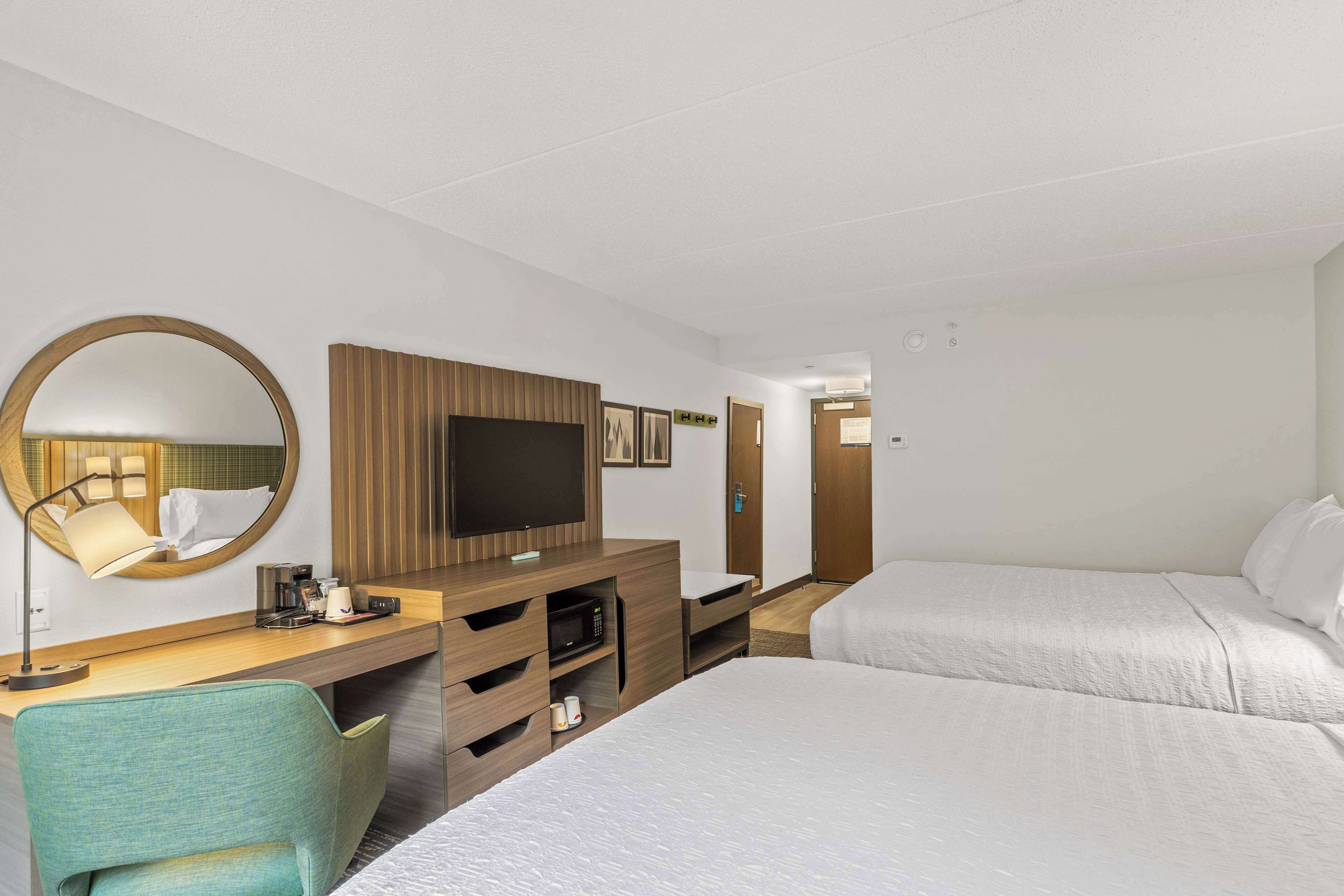 A hotel room with a bed, a desk with a television, a mirror, and a chair.