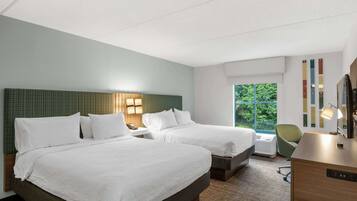 A hotel room with two beds, a desk, a chair, and a large window with a view of greenery.
