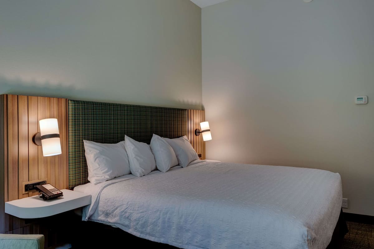 Quarto de hotel com uma cama grande, duas luminárias de cabeceira, um telefone e uma mesinha.