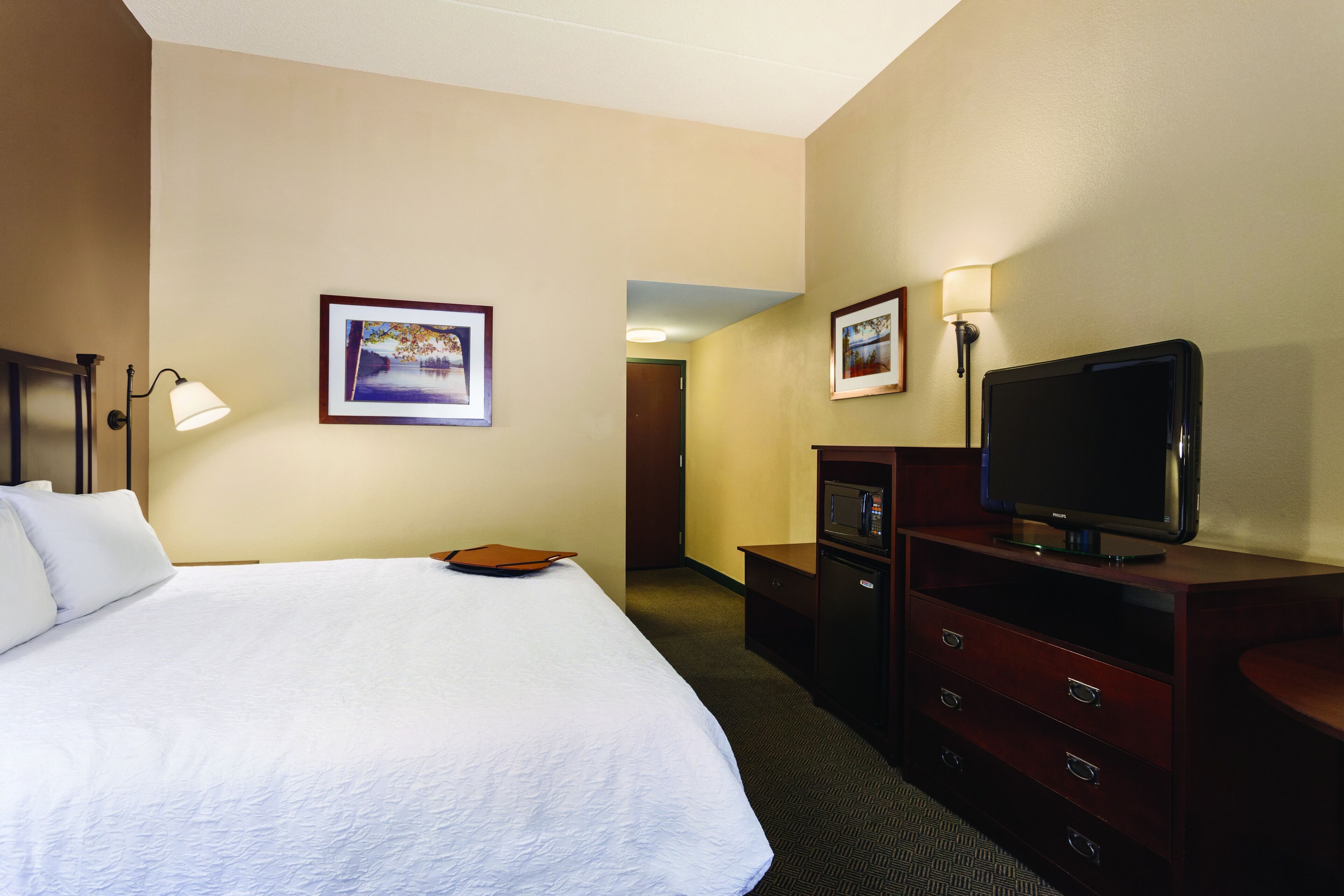 A hotel room with a large bed, a television, a desk, and two framed pictures on the wall.
